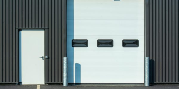 A modern industrial warehouse facade with a large white garage door and side entrance.