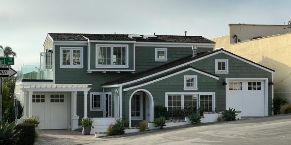 A stylish green two-story suburban house with white trim and garages on a sunny street corner.