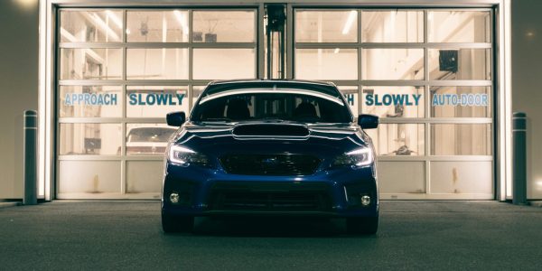 A sleek blue car parked in front of an illuminated service garage at night.